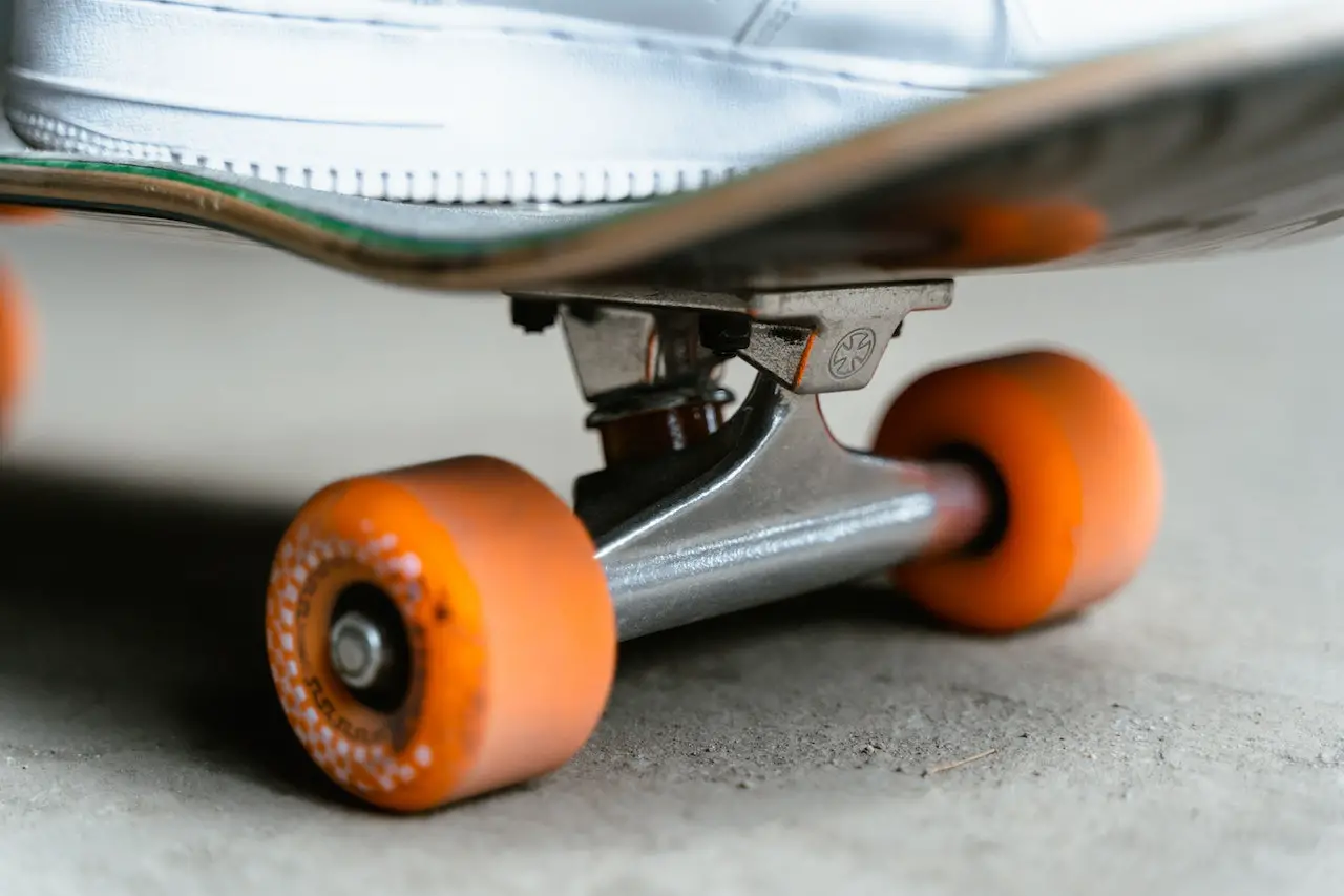 Image of a skate truck on a skateboard with orange wheels. Source: tima miroshnichenko, pexels