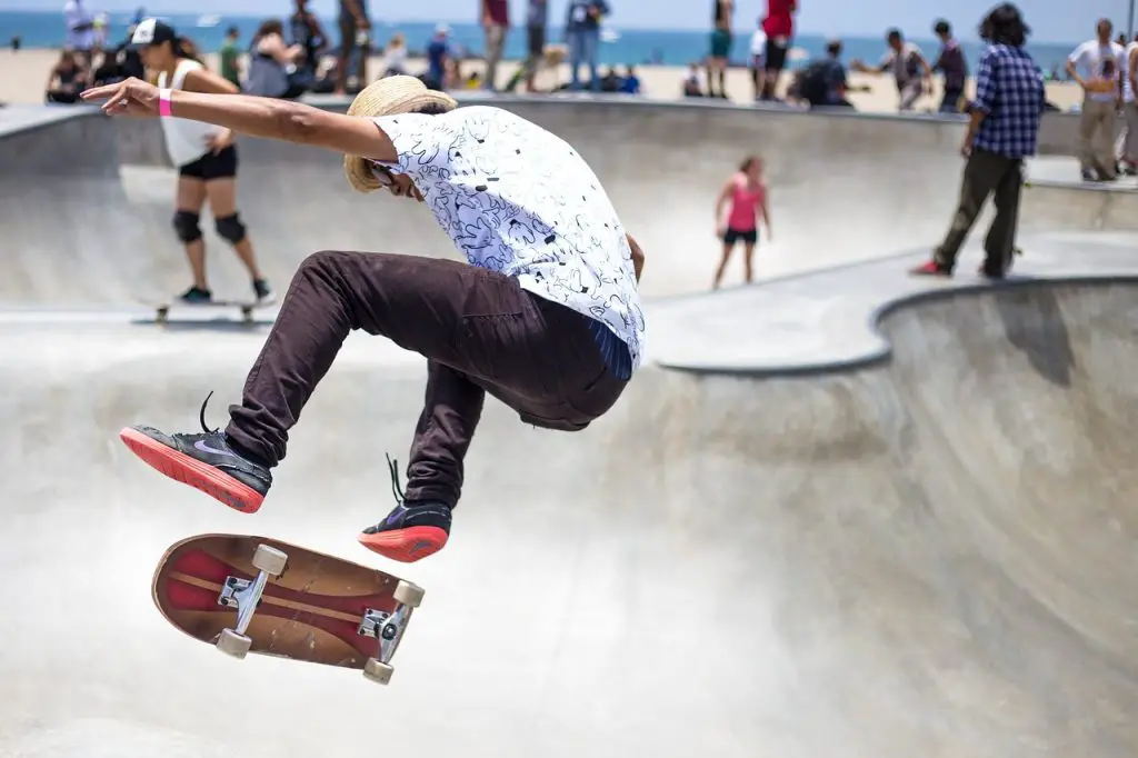 Image of a skateboarder wearing a white printed shirt and black pants doing freestyle skateboarding trick in a skate park. Source: pixabay