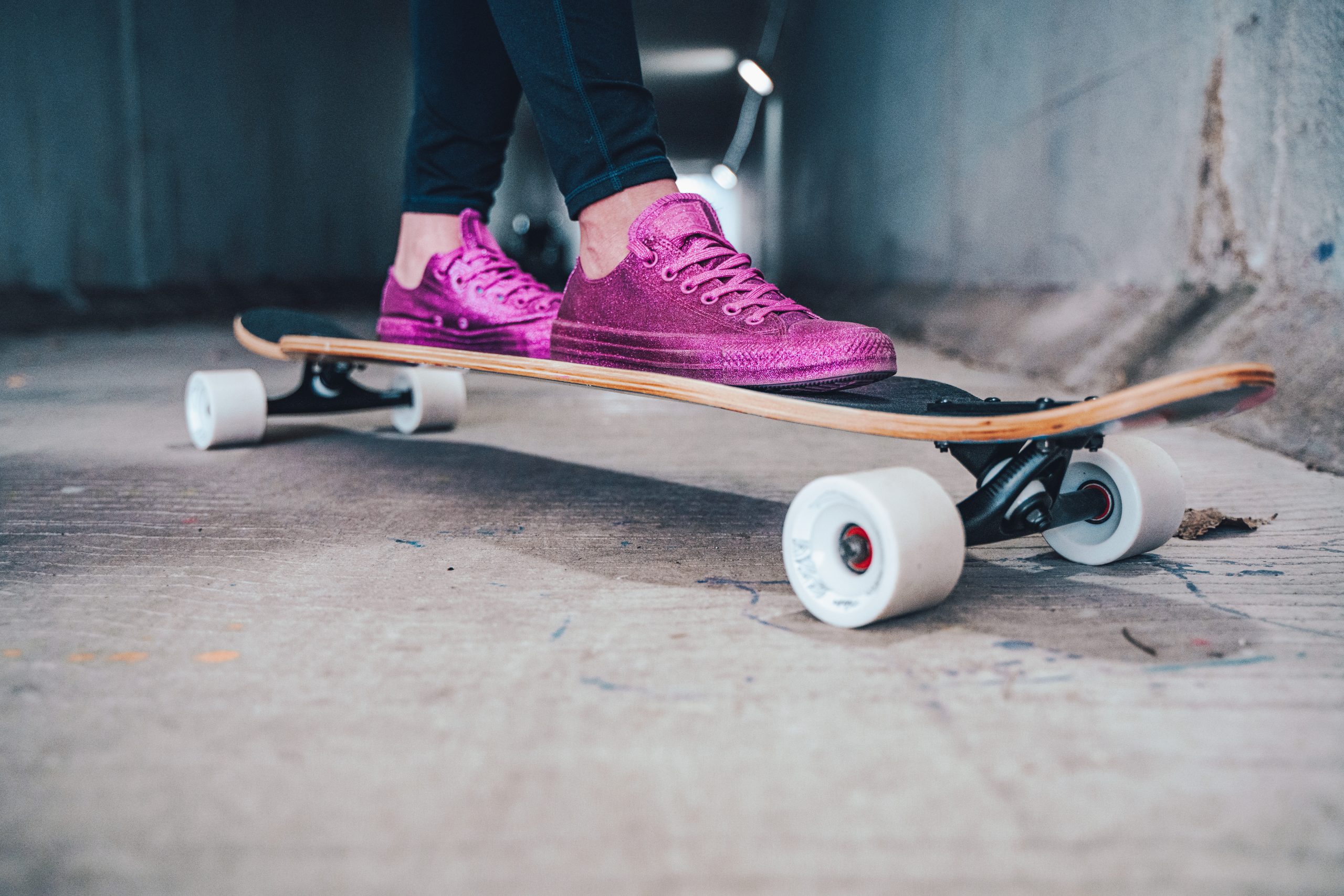Image of a skateboarder wearing jeans and pink shoes riding a black skateboard with white wheels. Source: chris haws, unsplash