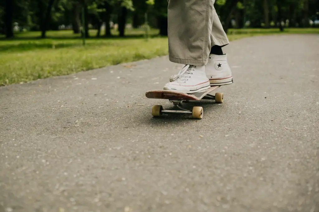 Image of a skateboarder wearing khaki pants and white converse shoes skateboarding on the street. Source: tima miroshnichenko, pexels