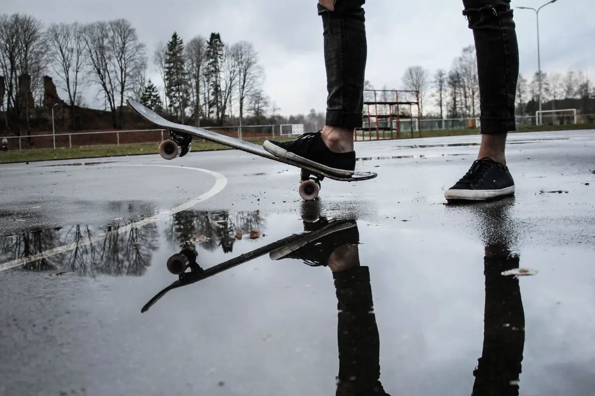 Image of a skateboarder in black jeans and a skateboard over a puddle in a court. Source: unsplash