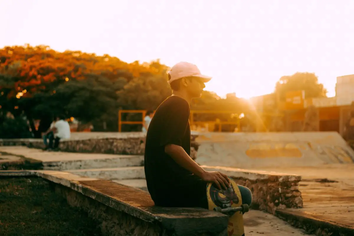 Image of a skateboarder sitting in a park while holding his skateboard.