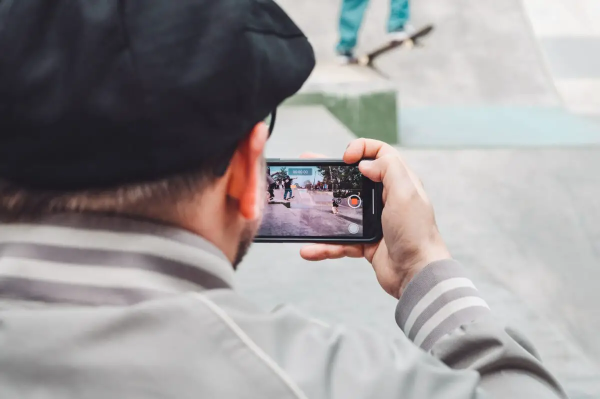 Image of a man holding a cellphone while watching a skateboarding video. Source: unsplash
