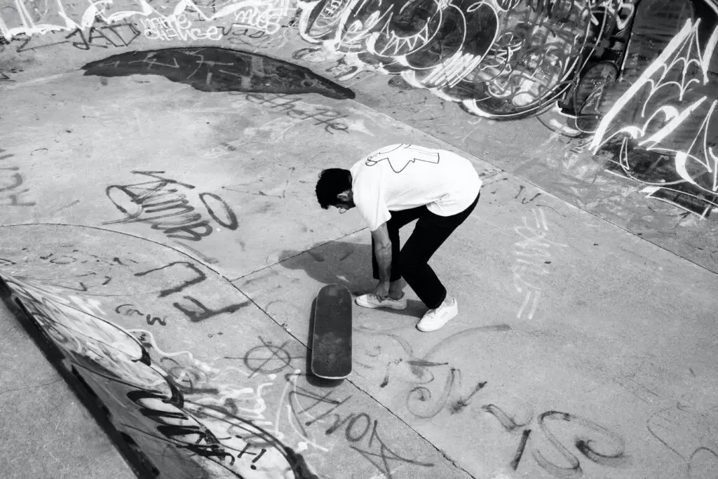 Image of a skateboarder tying his shoelace in a skate bowl.