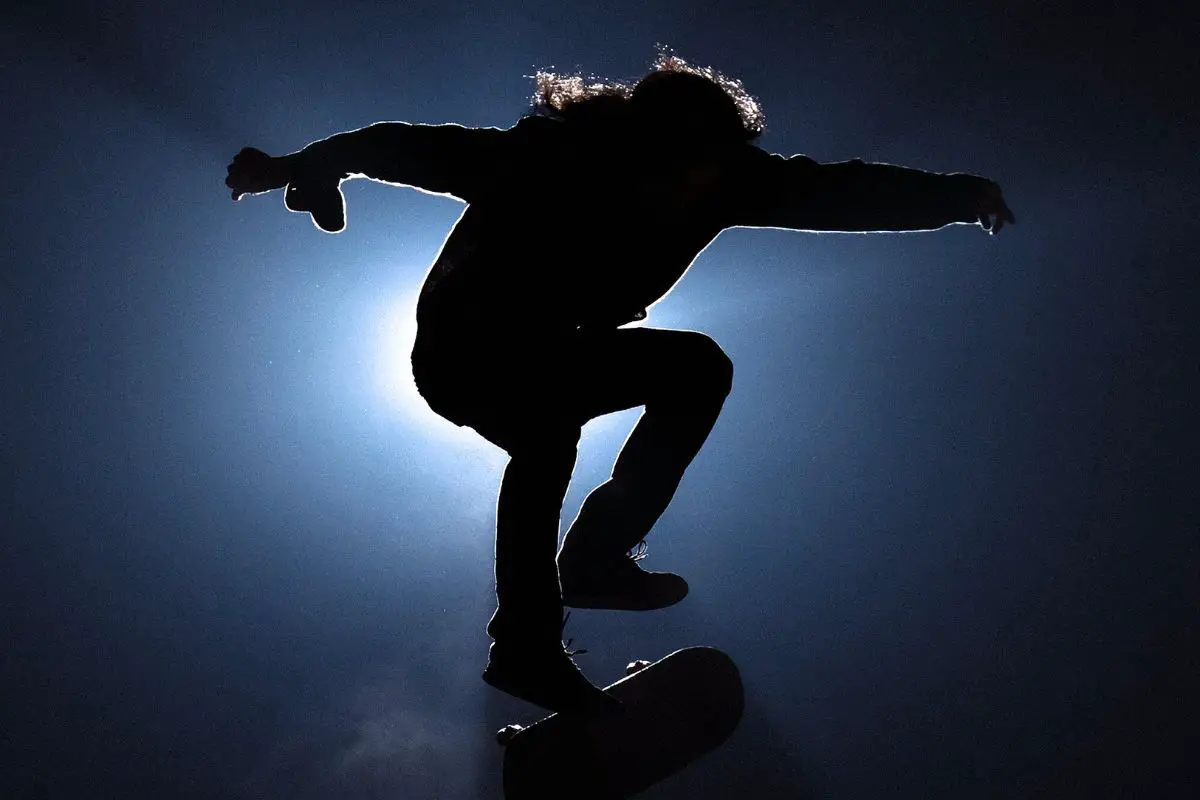 Image of a skater doing a freestyle skateboarding trick in the dark.